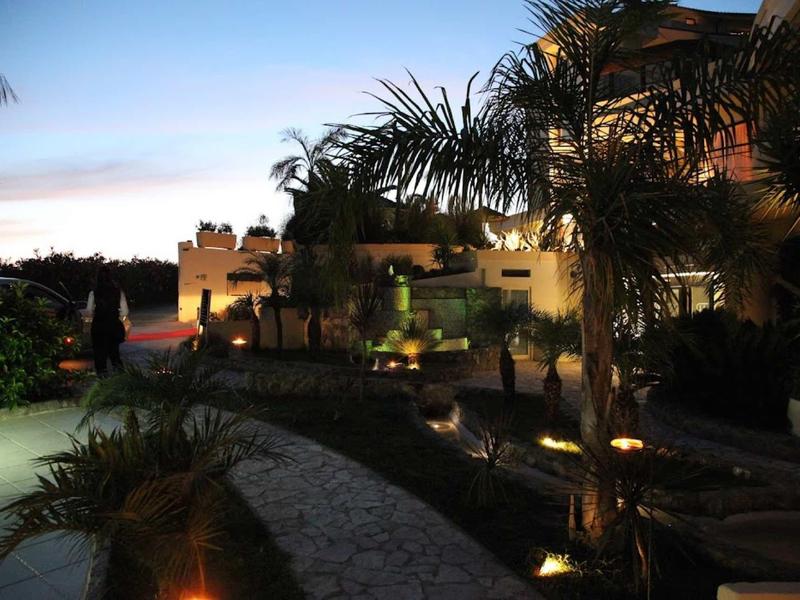 Večerní pohled na osvětlený hotel s palmami a dlážděnou cestou.