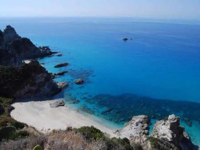 Pohled na odlehlou pláž s čistou modrou vodou a skalnatým pobřežím.