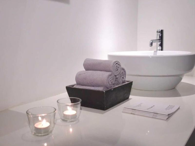 Moderní koupelnové zařízení s kulatým umyvadlem, ručníky a svíčkami na bílé ploše.