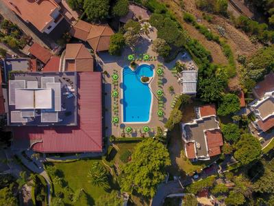 Vogelperspektive eines Hotels mit einem blauen Swimmingpool und umliegender grüner Vegetation.