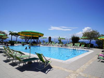 Ein klarer Pool mit Liegestühlen und Sonnenschirmen vor einem blauen Himmel und einer Meerblickkulisse.