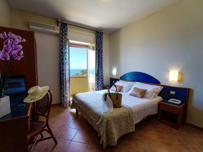 Gemütliches Hotelzimmer mit Doppelbett, Balkon und Blick aufs Meer bei Sonnenschein.