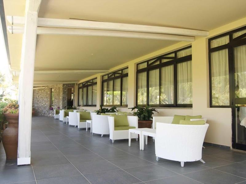 Overdekt hotelterras met witte fauteuils en kleine tafels langs de ramen.