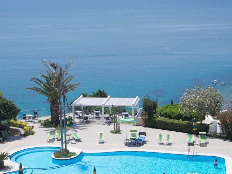 Hotelzwembad met palmbomen en wit paviljoen met uitzicht op de blauwe zee