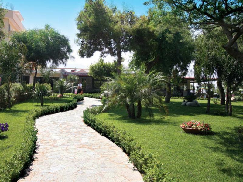 Gebogen wandelpad door groene tuin met bomen en bloemen onder een blauwe lucht.