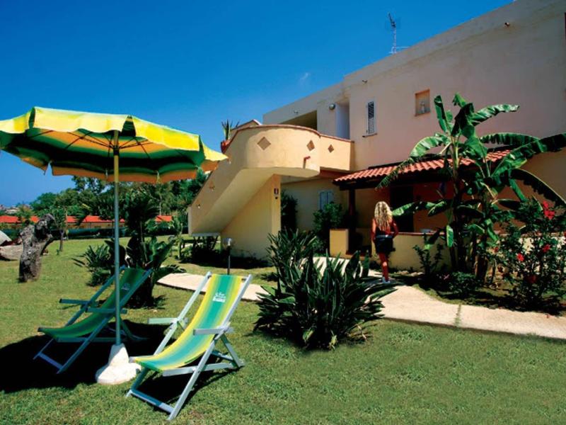 Zonnig tuinzicht met ligstoelen en parasol voor een wit gebouw.