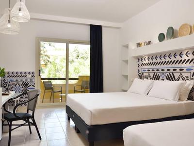 Camera d'hotel luminosa con letto matrimoniale, balcone e arredamento moderno.