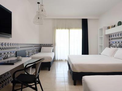 Camera d'albergo luminosa con due letti, scrivania, sedia e balcone con tende.