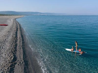 Tre persone che remano su un kayak in acqua limpida e blu vicino a una spiaggia di ciottoli.