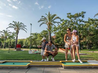 Quattro giovani giocano a mini golf in un'area verde e soleggiata con palme.