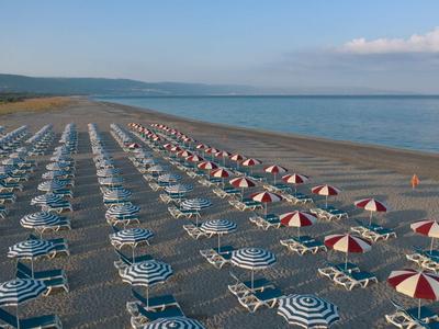 Spiaggia con file di ombrelloni colorati e lettini sulla riva.
