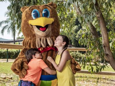 Bambini abbracciano un grande mascotte orso all'aperto con tempo soleggiato.