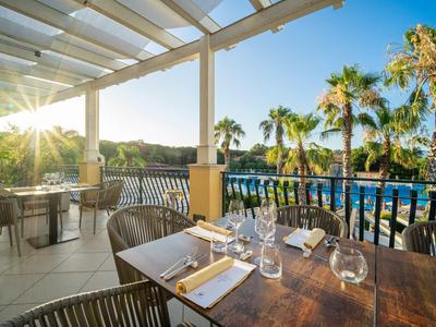 Terrazza con tavolo apparecchiato con vista su piscina e palme al tramonto.