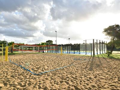 Piaszczyste boisko do siatkówki plażowej z siatką i przyległym basenem pod pochmurnym niebem.