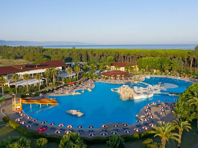 Grande piscina dell'hotel con lettini circostanti e vegetazione tropicale sotto un cielo terso.