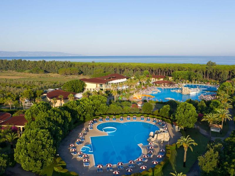 Grande hotel con più piscine, palme e vista sul mare sullo sfondo.