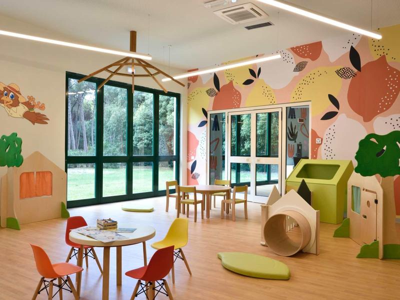 Sala giochi colorata per bambini con tavolo, sedie e decorazioni murali fantasiose.
