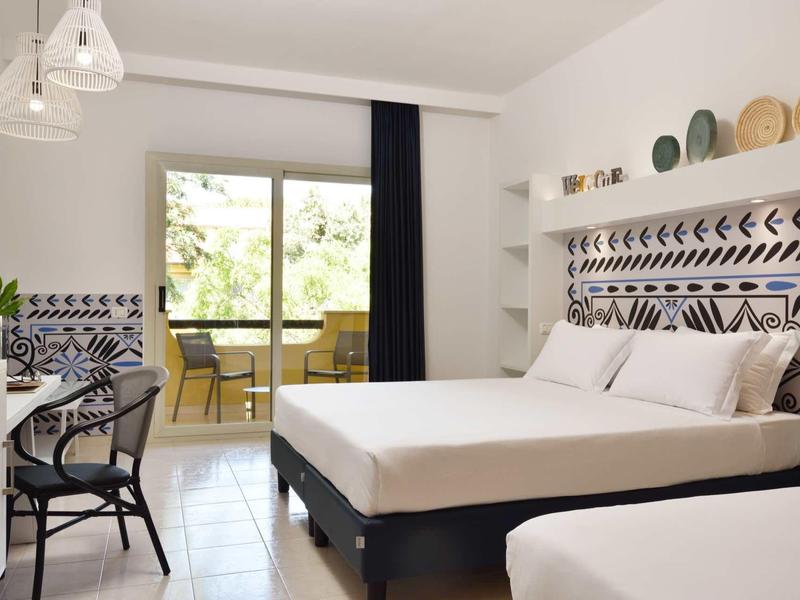 Camera d'hotel luminosa con letto matrimoniale, balcone e arredamento moderno.