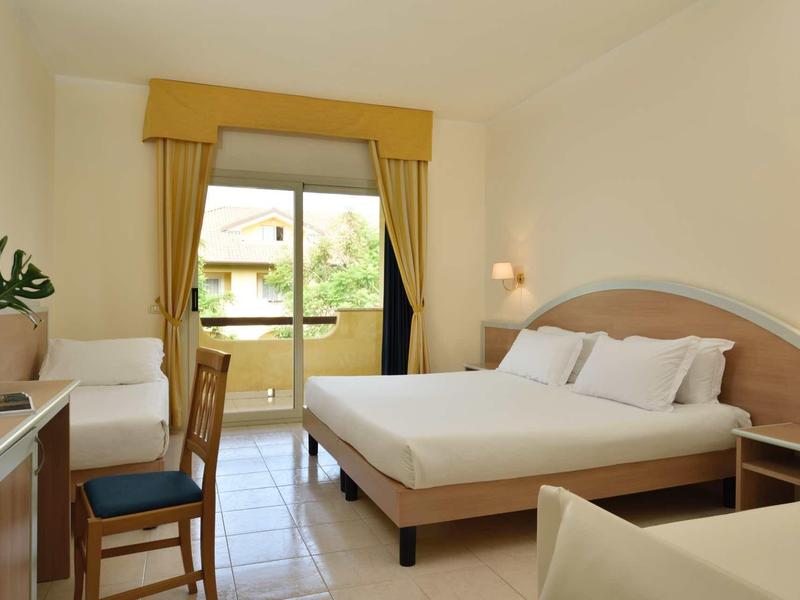 Camera d'hotel luminosa con letto matrimoniale, balcone e poltrona bianca.