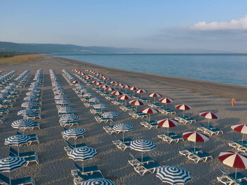 Spiaggia con file di ombrelloni colorati e lettini sulla riva.