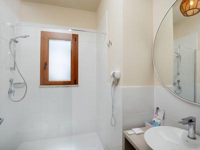 Moderne, wit betegelde badkamer met douche, wastafel en ronde spiegel.