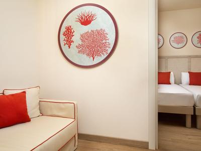 Lichte hotel gangkamer met bank en wanddecoratie met rode koraalmotieven.