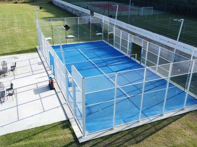 Moderne omheinde padelbaan naast een terras met tafels en stoelen op groen gras.