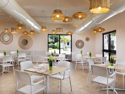 Lichte hotel eetruimte met witte stoelen, kleine tafels en geweven mandlampen aan het plafond.