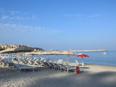 Sandstrand mit Reihen von Liegestühlen und Sonnenschirmen entlang eines ruhigen Meeres unter blauem Himmel.