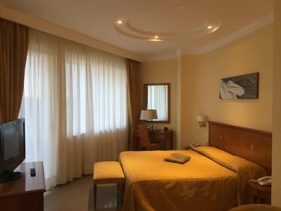 Gemütliches Schlafzimmer mit Doppelbett, gelben Bettdecke, Schreibtisch und TV vor großen Fenstern.