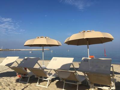 Leerer Strand mit Sonnenliegen und großen gelben Sonnenschirmen unter blauem Himmel.
