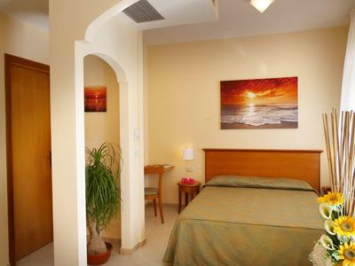 Gemütliches Schlafzimmer mit grünem Bett, Holzmöbeln, Pflanzen und Sonnenuntergang-Bild an der Wand.