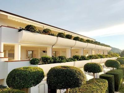 Moderner Gebäudekomplex mit weißer Fassade, mehreren Balkonen und kunstvoll geschnittenem Grün.