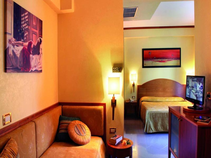 Gemütliches Hotelzimmer mit Sofa, Bett, TV, warmem Licht und einem roten Bild an der Wand.