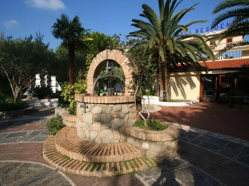 Ein steinerner Brunnen mit Bogen, umgeben von Palmen und einem sonnigen Patio.