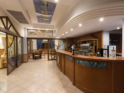 Moderner Hotelbarbereich mit geschwungenem Holzbar, Sitzgelegenheiten und beleuchtetem Deckenfenster.