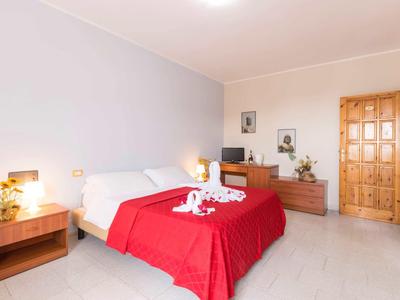 Chambre d'hôtel lumineuse avec lit double, couvertures rouges et meubles en bois près d'une porte en bois.