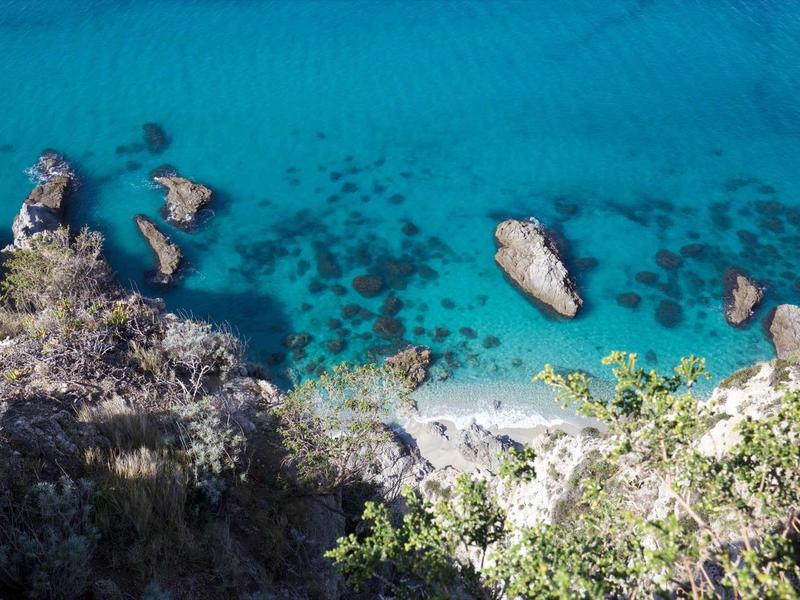 Eau turquoise claire et plage rocheuse vue d'en haut avec végétation au premier plan.