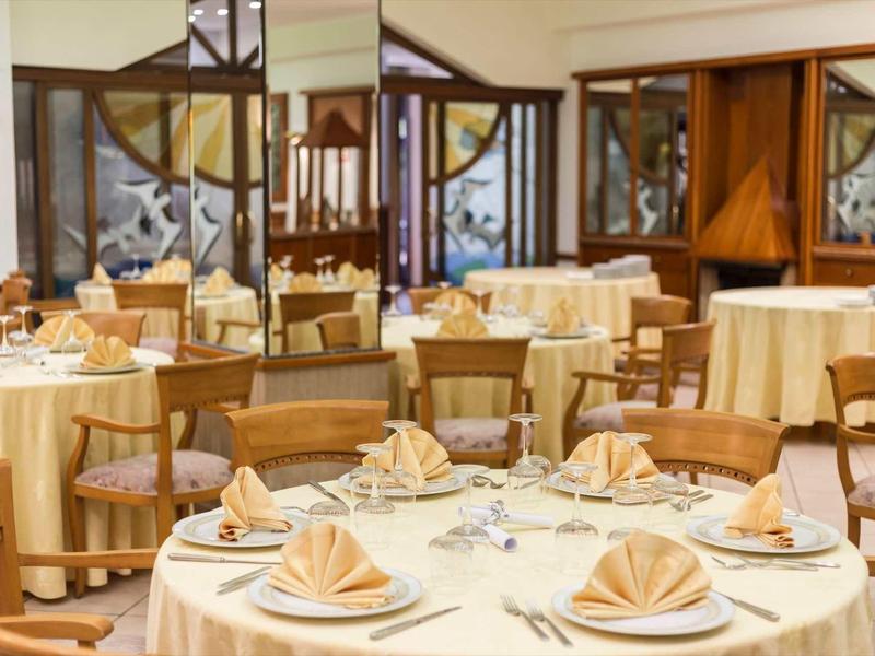 Salle à manger élégante avec des tables rondes, nappes beiges et serviettes soigneusement pliées.