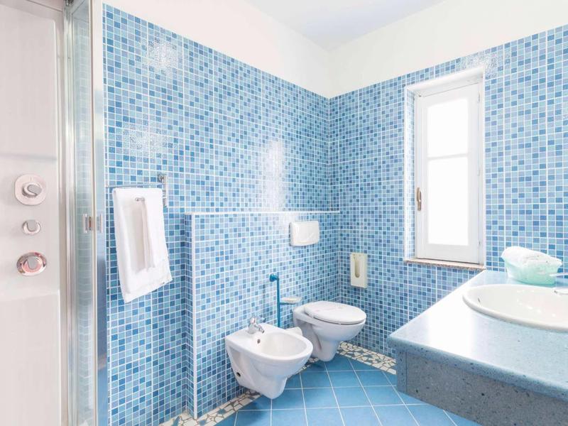 Salle de bain lumineuse avec carrelage bleu, toilettes, bidet, lavabo et fenêtre.