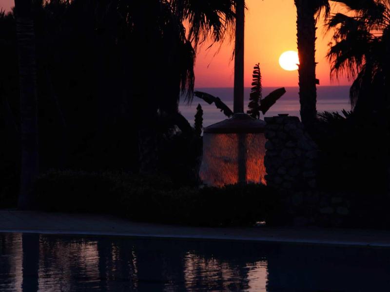 Coucher de soleil sur la mer avec des palmiers et une piscine au premier plan.