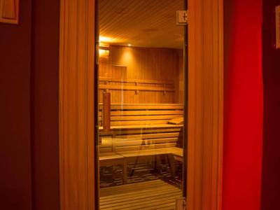 Salle de sauna moderne avec revêtement en bois et porte vitrée sous lumière chaude.
