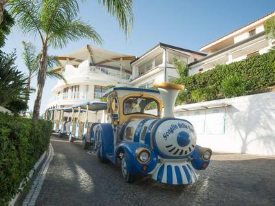 Kleiner blauer Touristenzug fährt an einer Hotelanlage mit Palmen entlang.