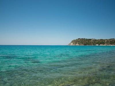 Mer turquoise claire avec côte rocheuse et cap végétalisé sous ciel bleu.