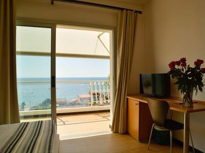Chambre d'hôtel avec bureau, chaise, télévision et vue sur la mer par la porte terrasse.