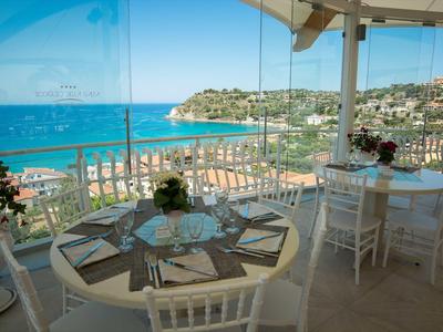 Überdachte Terrasse eines Restaurants mit Blick auf das Meer und Tische mit weißen Stühlen.