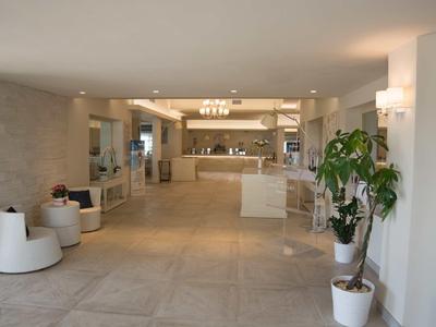 Hall d'hôtel lumineux et moderne avec sol en marbre, réception et plantes.