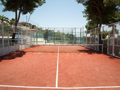 Leerer Tennisplatz mit rotem Sandboden und weißen Linien, umgeben von Zäunen und Bäumen.