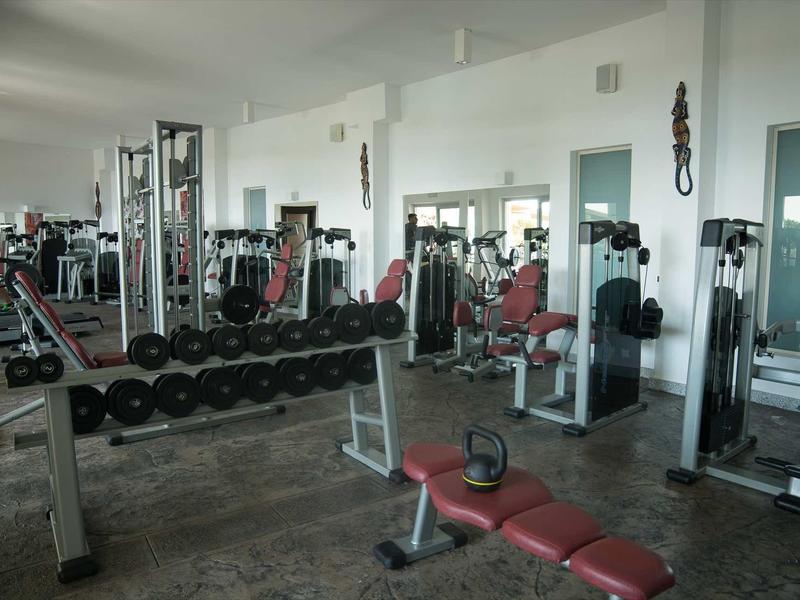 Salle de sport moderne avec haltères, machines de musculation et miroirs dans une pièce lumineuse.