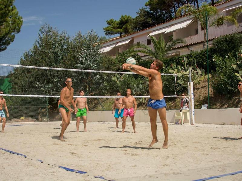 Des gens jouent au beach-volley sur un terrain de sable à côté d'un hôtel sous le soleil